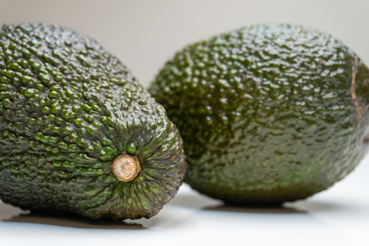 Detailed close-up of two fresh avocados on a white surface, showcasing texture and healthy green color.
