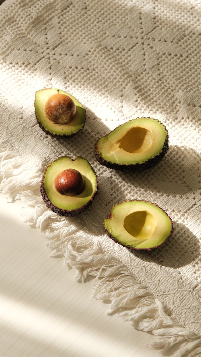 Fresh halved avocados displayed on a sunlit, textured cloth perfect for culinary presentations.